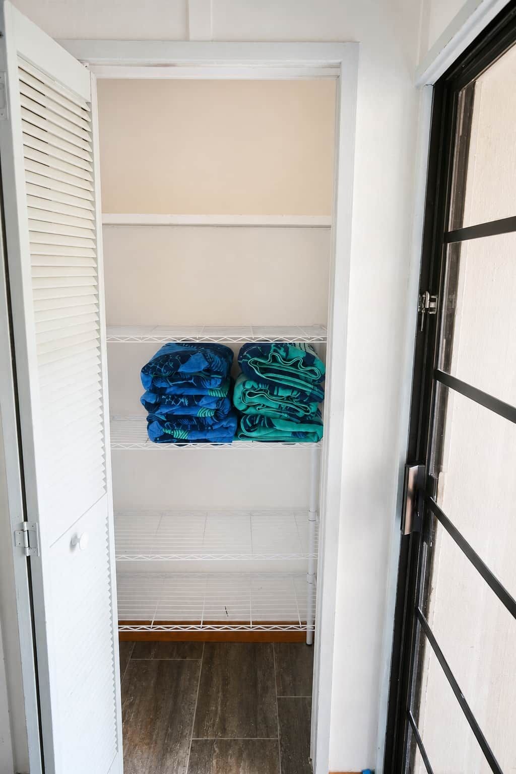 A walk-in closet with white shelving, a door with a black frame, and a tiled floor.
