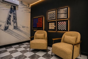 Ein Zimmer mit Schachbrettmuster auf dem Boden, zwei beige Sessel und einer Wand mit Schachbrett-Design, sowie eine große Klimaanlage.