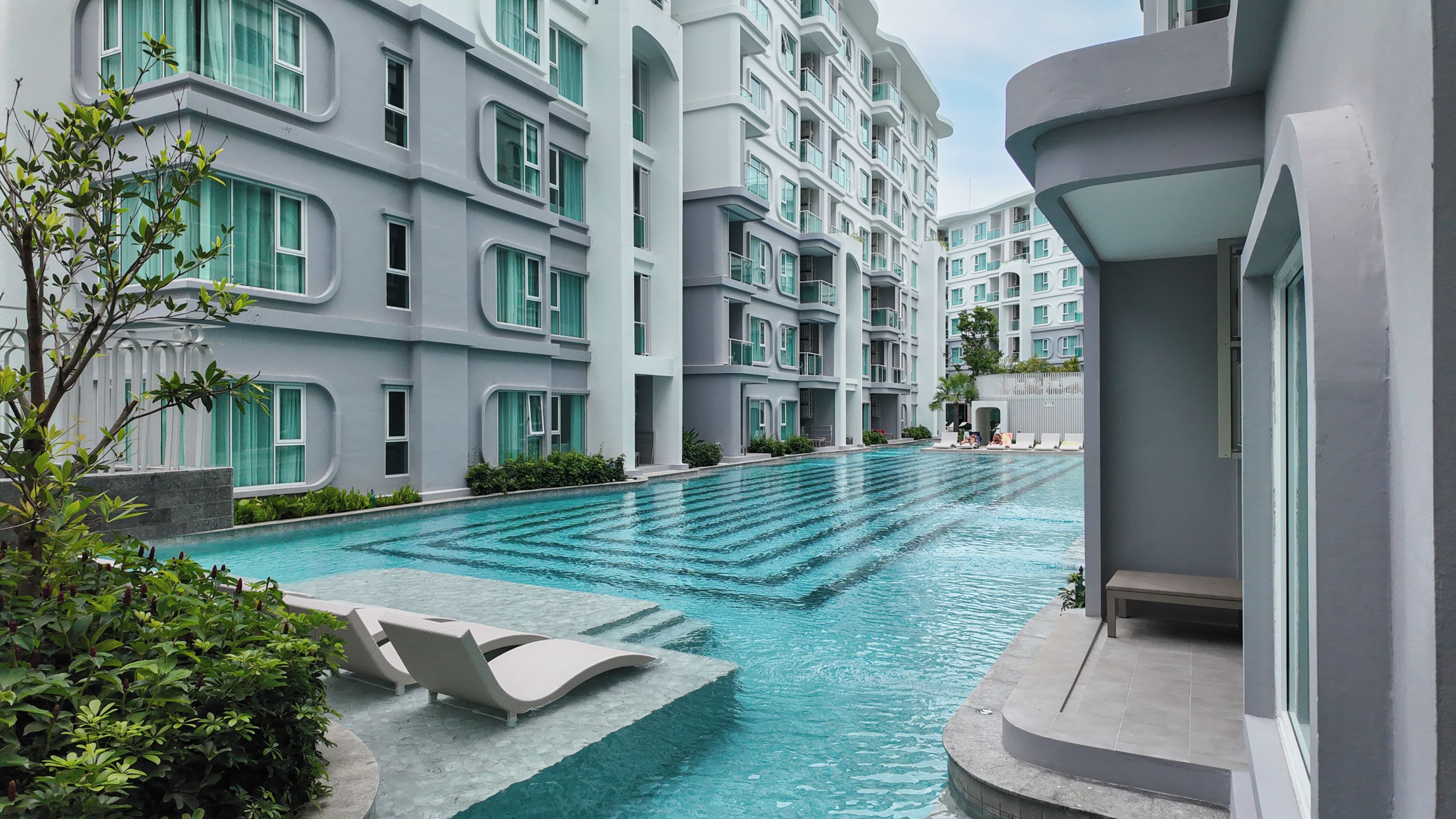 Un edificio moderno con piscina, sillas de descanso y un jardín bien cuidado.