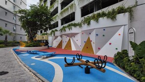 Une aire de jeux dotée de murs d’escalade aux couleurs vives et d’un sol en caoutchouc bleu, entourée d’un bâtiment aux murs blancs et agrémentée de verdure.