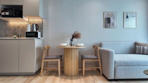 Une cuisine moderne équipée d’un four à micro-ondes, d’une bouilloire et d’une machine à café, une table à manger avec deux chaises et un canapé gris.