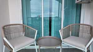 Two wicker chairs with cushions, a small round table, and a view through a glass door. - Lumi 1br suite | Title Serenity Nai Yang (Tambon Sa Khu)
