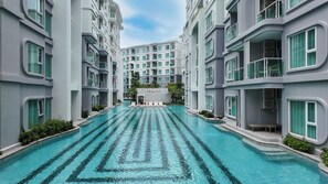 A modern hotel with a central swimming pool, multiple balconies, and a contemporary architectural design. - Lumi 1br suite | Title Serenity Nai Yang (Tambon Sa Khu)