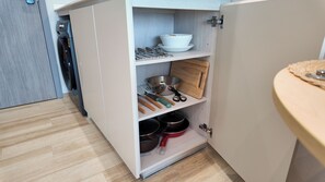 Une cuisine équipée d’un lave-vaisselle intégré, d’une planche à découper en bois et de divers ustensiles rangés sur les étagères.
