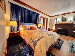 A hotel room with a large bed, two bedside lamps, a fireplace, and a framed picture on the wall. - Wonderful 2-bedroom apartment in The Handsome Craftsman in Highland Square (Akron)