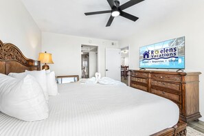 A hotel room with a bed, a wooden dresser, a television, and a ceiling fan. - Bay Beach Retreat with Pool, Spa, Tennis, Pickleball and Waterfront Family Fun - Bay Beach - Roelens (Fort Myers Beach)