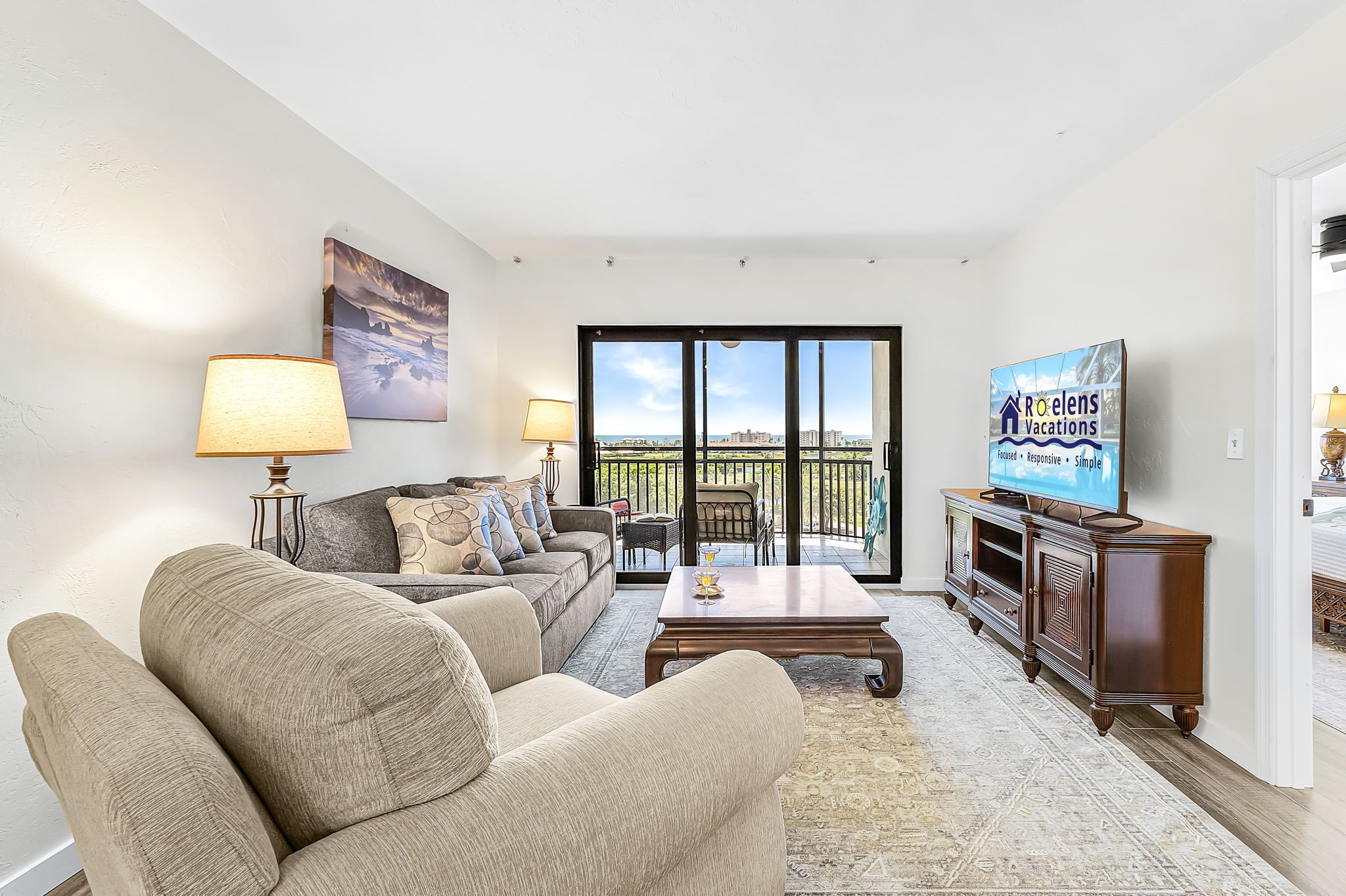 A living room with a sofa set, a coffee table, a TV, and a balcony with a view.