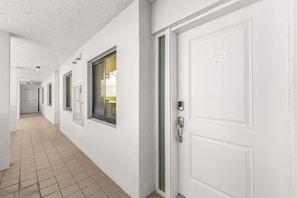 A corridor with white walls, a tiled floor, and doors numbered 713. - Bay Beach Retreat with Pool, Spa, Tennis, Pickleball and Waterfront Family Fun - Bay Beach - Roelens (Fort Myers Beach)