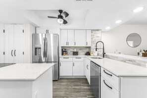 A modern kitchen with white cabinetry, a stainless steel refrigerator, a built-in oven, a coffee maker, and a sink with a modern faucet. - Bay Beach Retreat with Pool, Spa, Tennis, Pickleball and Waterfront Family Fun - Bay Beach - Roelens (Fort Myers Beach)