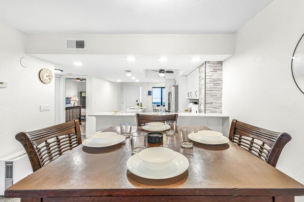 Cozinha moderna com armários brancos, uma mesa de jantar posta para quatro pessoas e vista para a sala de estar.