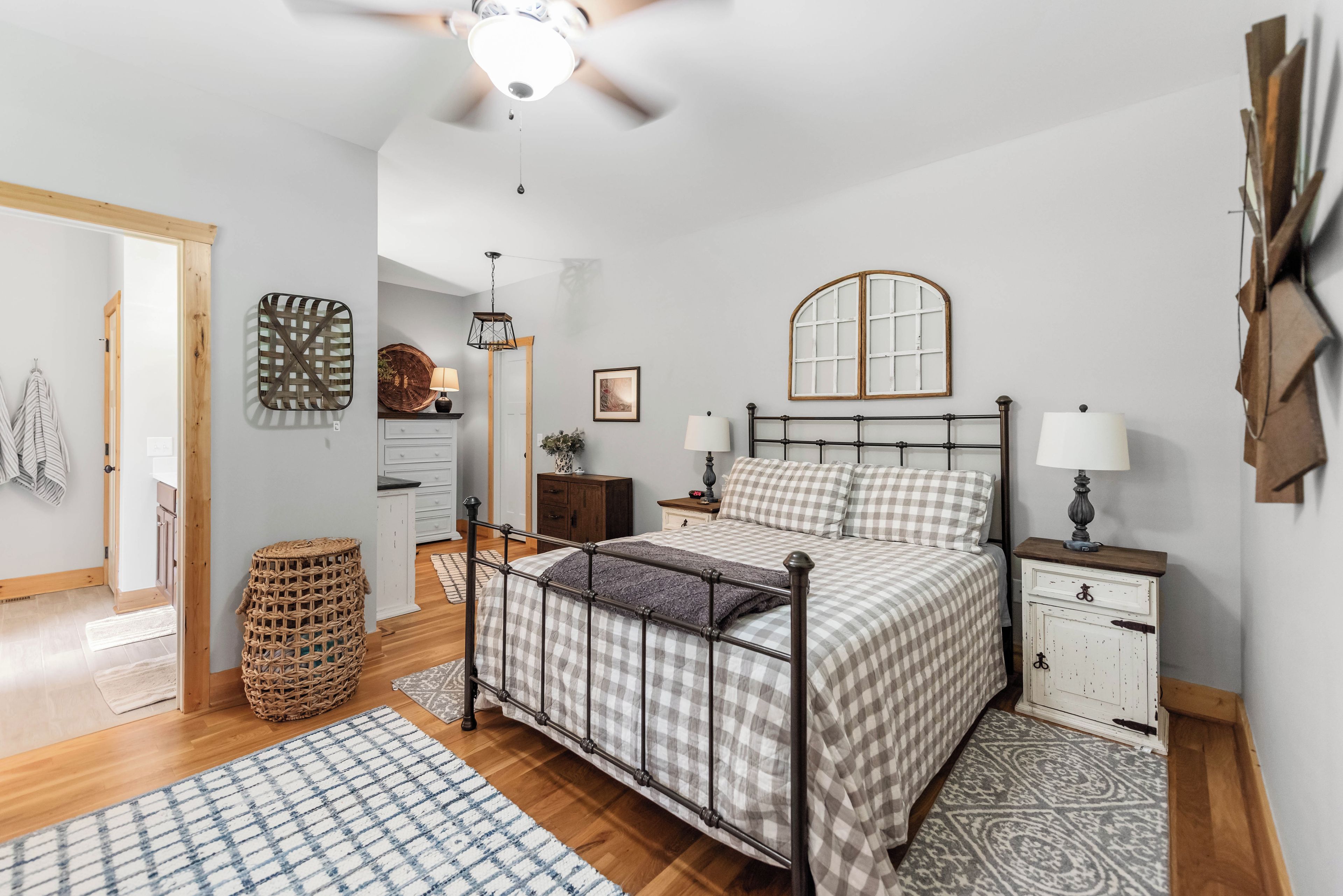 A bedroom with a bed, bedside tables, a nightstand, a hanging lamp, a ceiling fan, a woven basket, and a patterned rug.