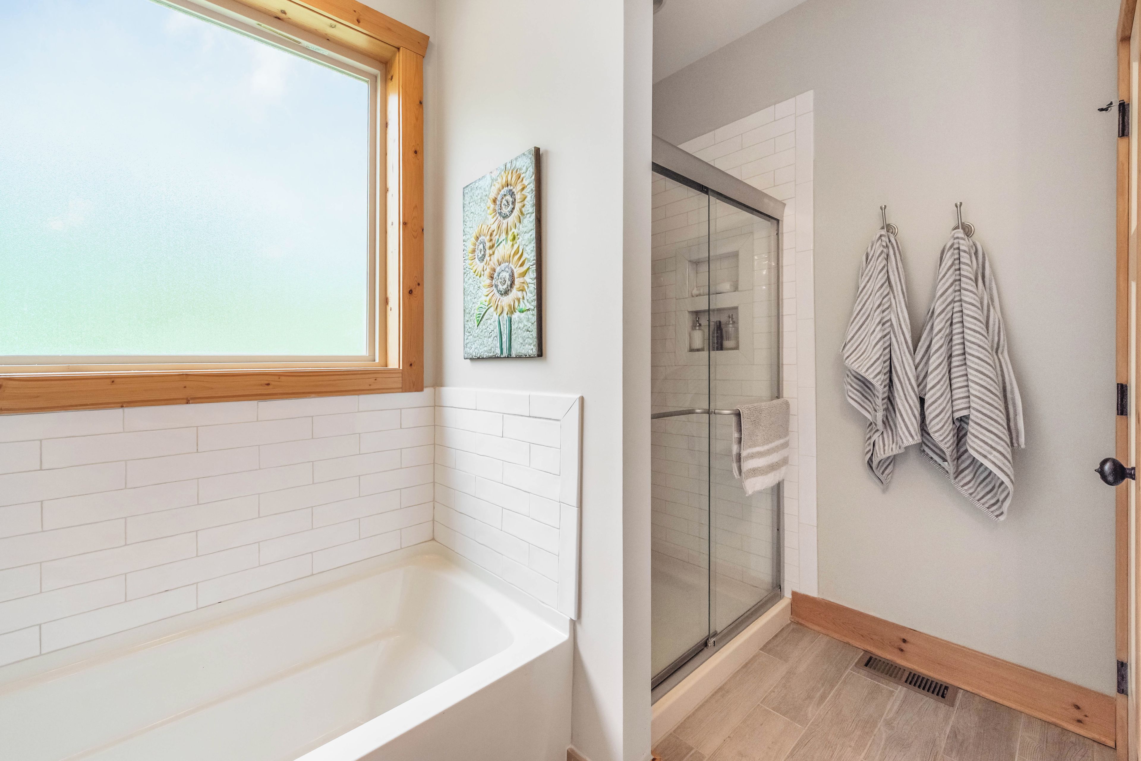 A bathroom with a white bathtub, a glass shower enclosure, and two striped towels hanging on hooks.