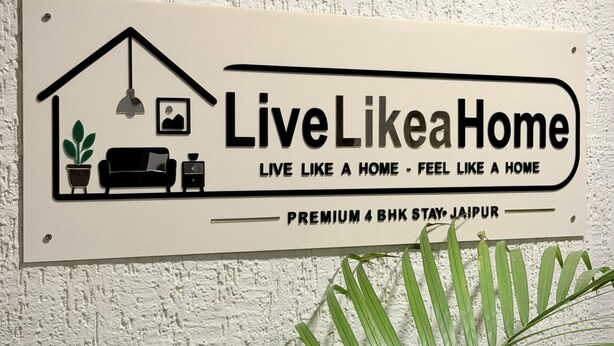 Um letreiro com o texto 'LiveLikeaHome' e 'ESTADIA PREMIUM DE 4 QUARTOS JAIPUR' em uma parede texturizada.