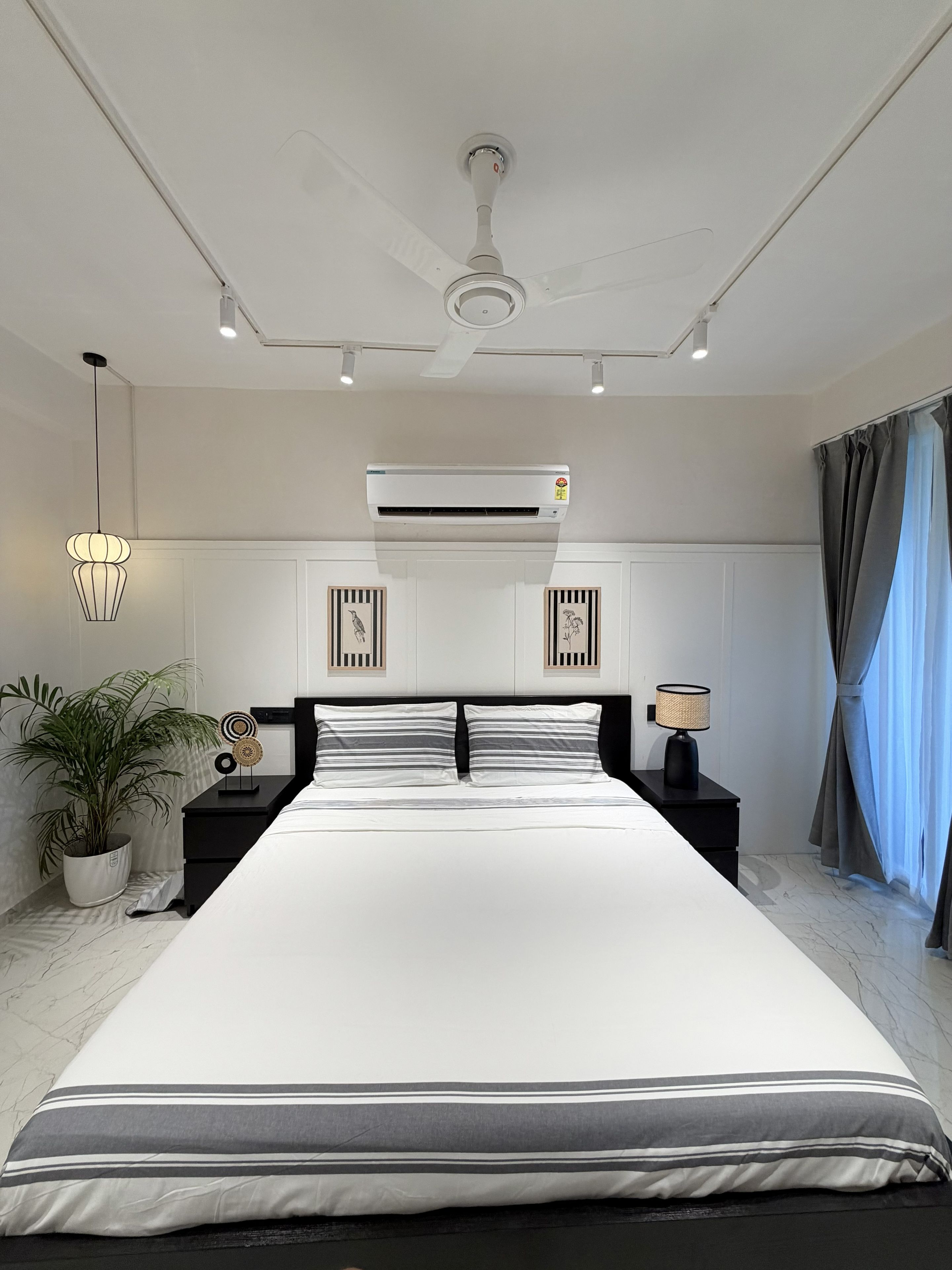Une chambre moderne avec un grand lit, un ventilateur de plafond, un climatiseur, une lampe de chevet et une plante en pot.