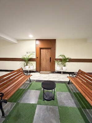 Una zona de recepción con dos bancos de madera, una mesita redonda y plantas en macetas.