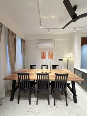 A modern dining area with a wooden table, black chairs, a ceiling fan, and an air conditioning unit. - LiveLikeaHome | Your Spacious 4 BHK Jaipur Home (Jaipur)
