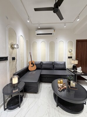 Una sala de estar moderna con un sofá seccional, una mesa de centro redonda, una guitarra y un ventilador de techo.