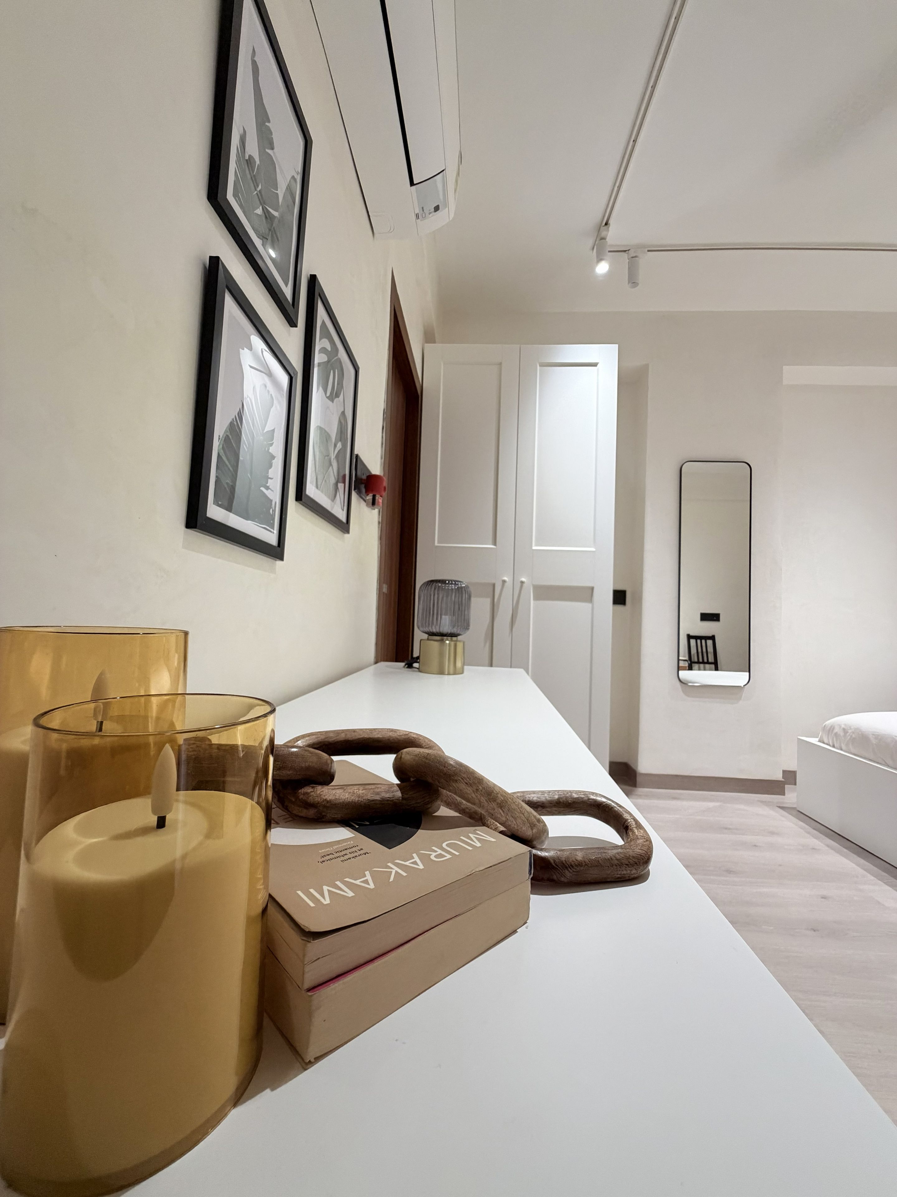 A modern bedroom with a white bed, a large mirror, and a wooden sculpture on the nightstand.