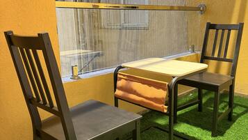 A room with a table and two chairs, a window with metal bars, and artificial green grass flooring.
