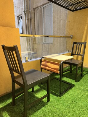 A room with a table and two chairs, a window with metal bars, and artificial green grass flooring. - LiveLikeaHome | Your Spacious 4 BHK Jaipur Home (Jaipur)