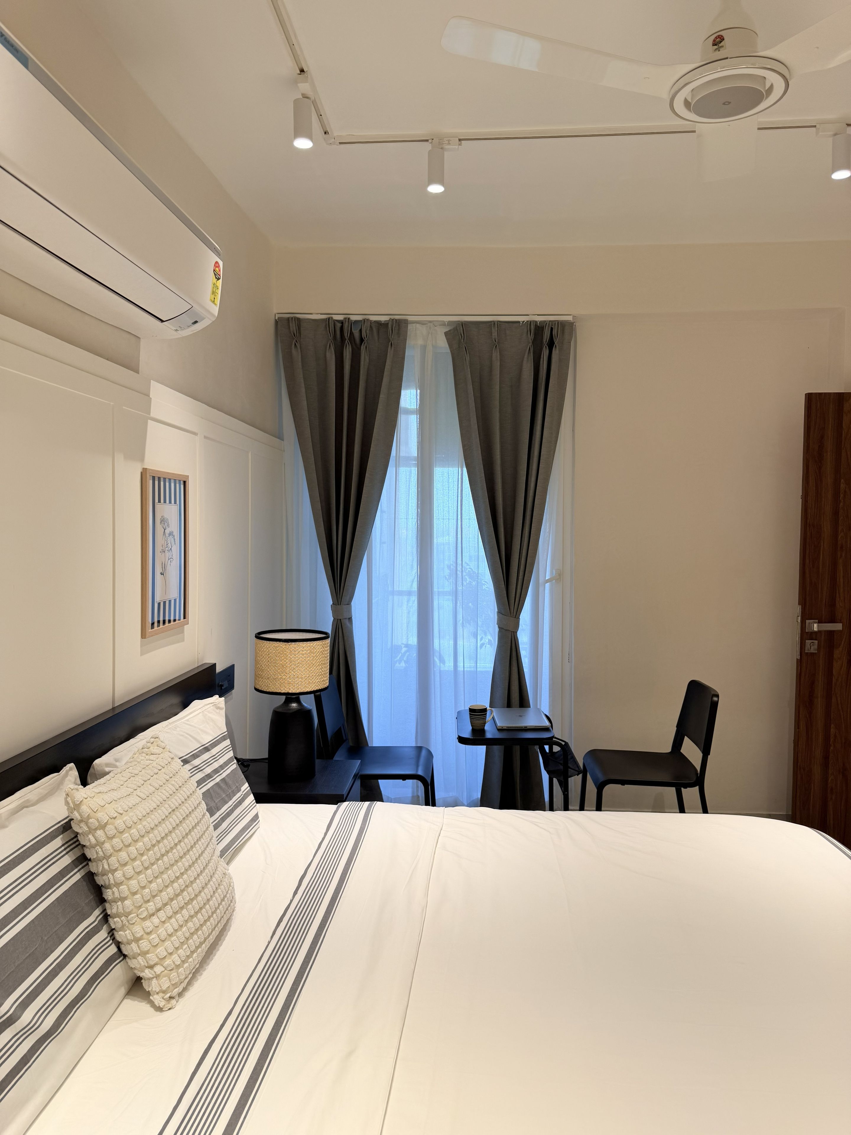 Ein Hotelzimmer mit einem großen Bett, einem Schreibtisch mit Stuhl, einer Lampe und einem fenster mit Vorhängen.