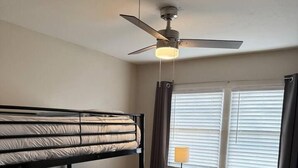 Una stanza con un letto a castello, una scrivania, una sedia e una ventola a soffitto.