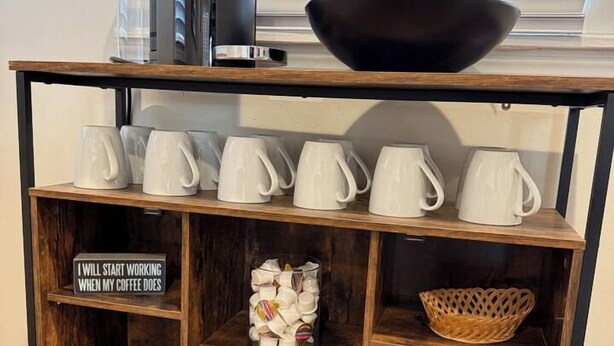 Un tavolino in legno con una macchina per il caffè, una ciotola nera e tazze bianche.