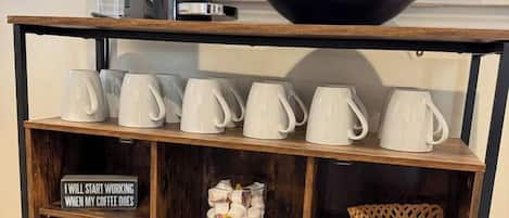 A wooden coffee table with a coffee maker, a black bowl, and white mugs.