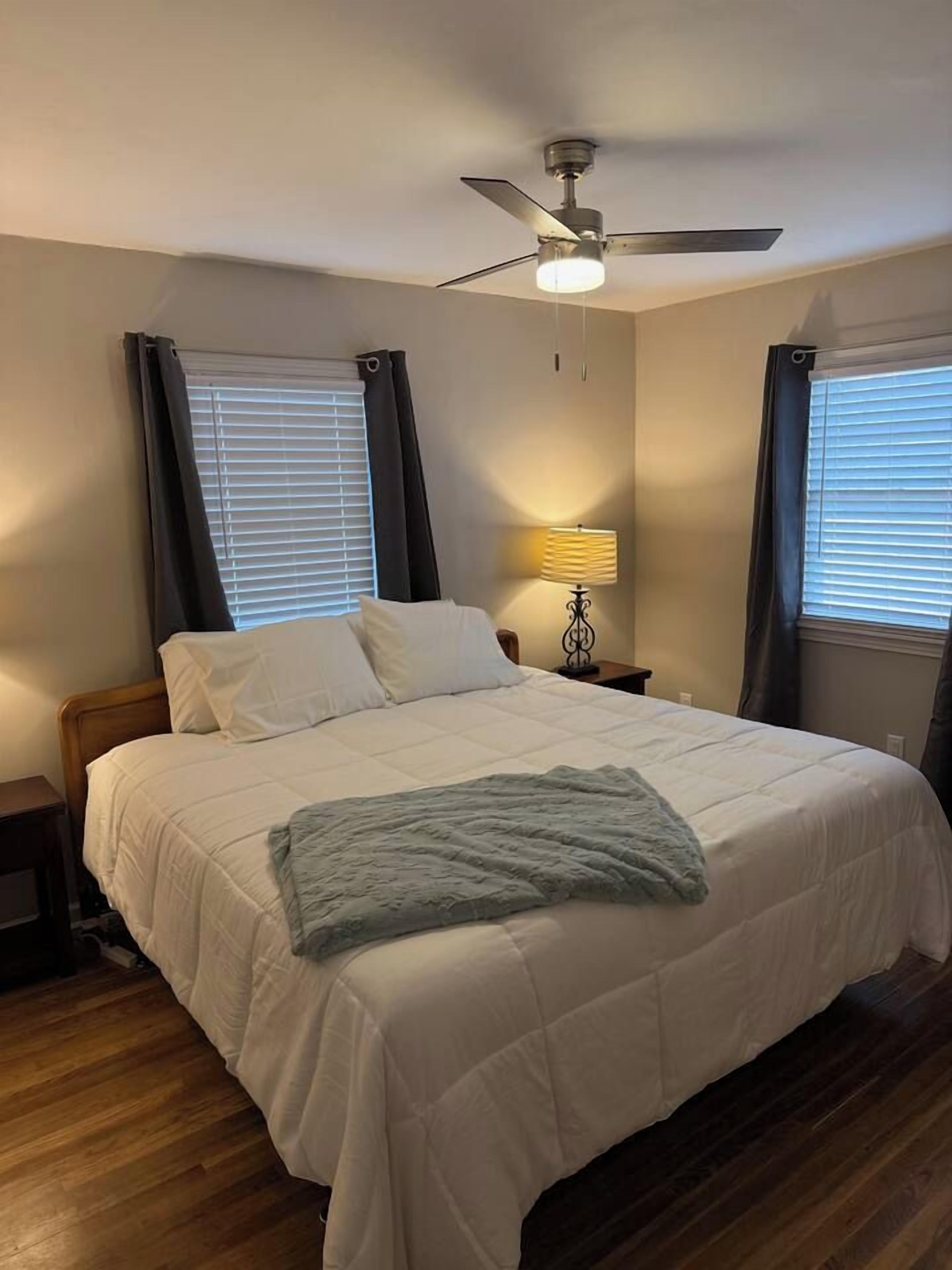 Une chambre à coucher avec un lit, un ventilateur de plafond, une lampe de chevet et une fenêtre avec des rideaux.