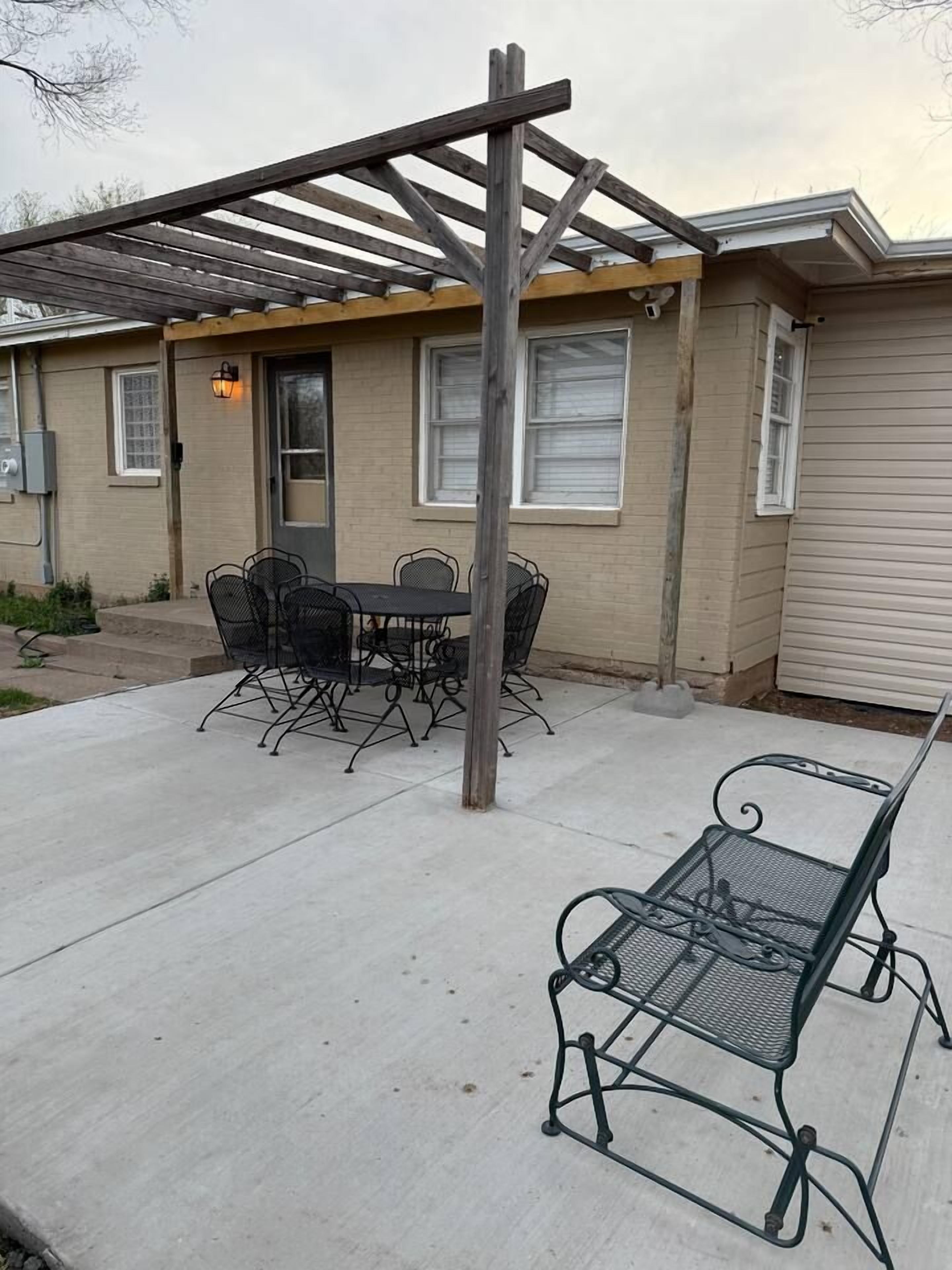 Un espace patio agrémenté d’une pergola, d’une table à manger avec des chaises et d’un banc en métal.