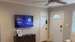 Un soggiorno con TV a schermo piatto, ventilatore a soffitto, tavolino in legno e divano beige.