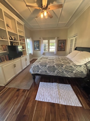 A bedroom with a bed, a ceiling fan, a television, and a bookshelf.