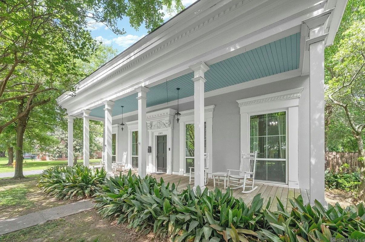 A white building with a covered porch, columns, and a number '2103' on the door.