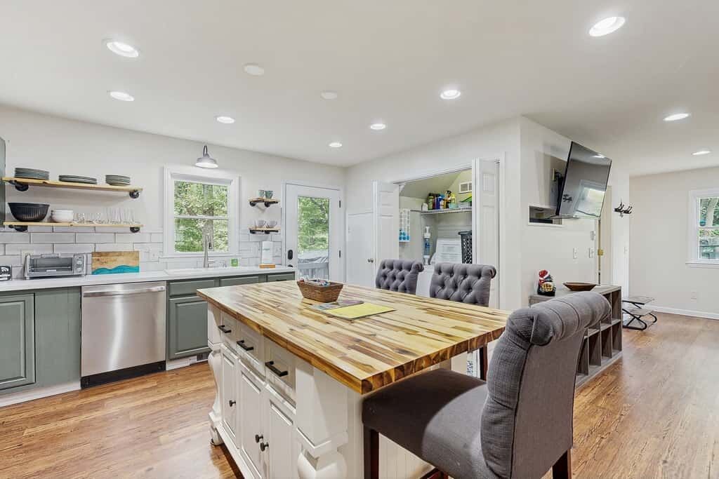 A modern kitchen with a central island, built-in appliances, and a dining area with a grey upholstered chair.