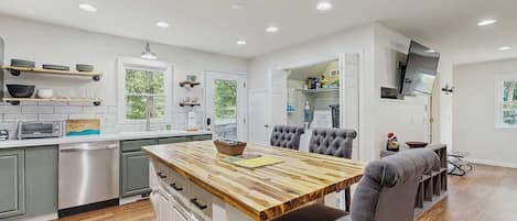 A modern kitchen with a central island, built-in appliances, and a dining area with a grey upholstered chair.