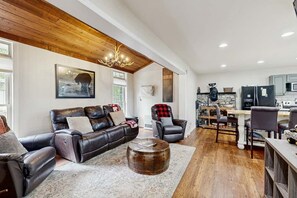A spacious living room with a leather sofa, a coffee table, and a dining area with chairs and a table. - Three Bears Cabin | Hot Tub, Pet Friendly, Minutes from Blowing Rock (Blowing Rock)