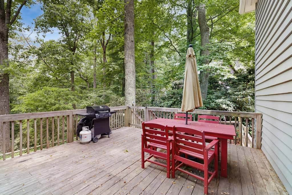 Een houten terras met een rode tafel en stoelen, een barbecue en een propaantank.
