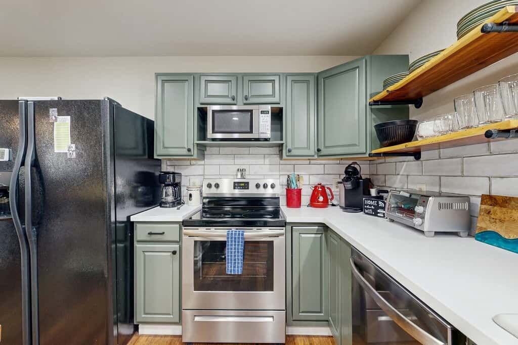 A kitchen with stainless steel appliances, green cabinets, and a white countertop.