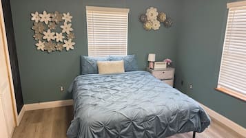 Un dormitorio con cama, mesita de noche, adornos en la pared y una ventana con persianas.