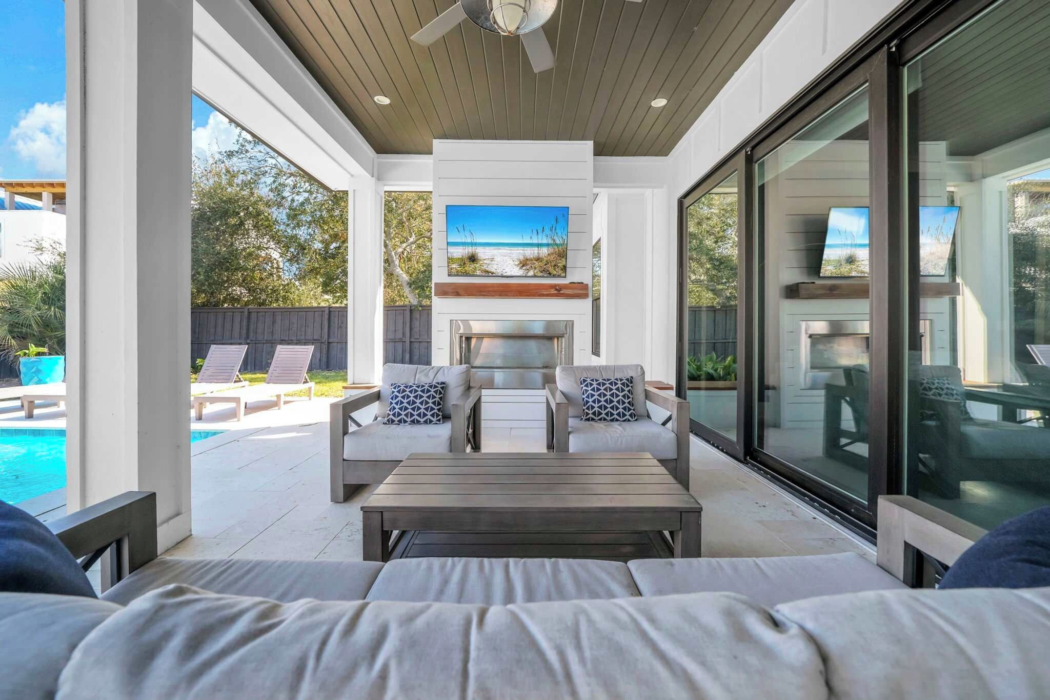 An outdoor patio with a pool, a seating area with cushions, and a fireplace.