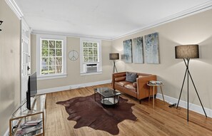 A living room with a leather sofa, a glass coffee table, a cowhide rug, a television on a stand, and artwork on the walls.