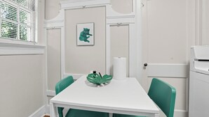 A white table with a green chair, a framed picture, and a roll of paper towels.