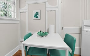A white table with a green chair, a framed picture, and a roll of paper towels.