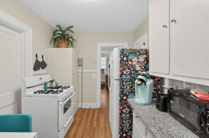 A compact kitchen with white cabinetry, a gas stove, a microwave, and a coffee maker.