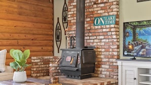 A cozy room with a brick fireplace, a wooden wall, and a framed picture of a cabin. - Lake and Ski/Gameroom/Dogrun (Wofford Heights)