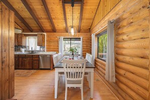 A wooden cabin interior with a dining area, kitchen, and large windows. - Lake and Ski/Gameroom/Dogrun (Wofford Heights)
