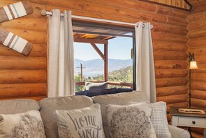 A log cabin interior with a sofa, a view of mountains, and a wooden ceiling. - Lake and Ski/Gameroom/Dogrun (Wofford Heights)