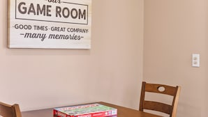 A wooden sign with text welcoming to a game room, a Monopoly board game on a table, and two wooden chairs. - Lake and Ski/Gameroom/Dogrun (Wofford Heights)
