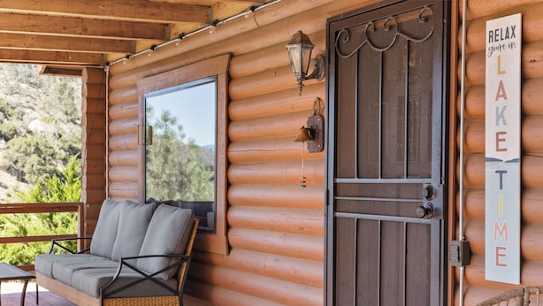 A log cabin with a porch, a wicker chair, a window, a door with a metal gate, and a sign that reads 'RELAX you're on LAKE TIME'. - Lake and Ski/Gameroom/Dogrun (Wofford Heights)