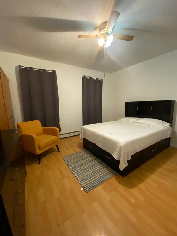 Un dormitorio con cama, ventilador de techo, una silla y cortinas.